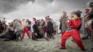 Une bande de musiciens et de carnavaleux sur la plage de Malo les bains dansant et jouant sous un ciel orageux.