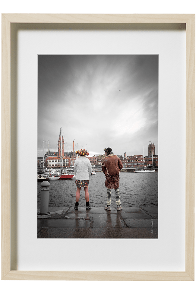 Deux carnavaleux face à la ville de Dunkerque, urinent dans le port à coté d'une bitte d'amarrage.
