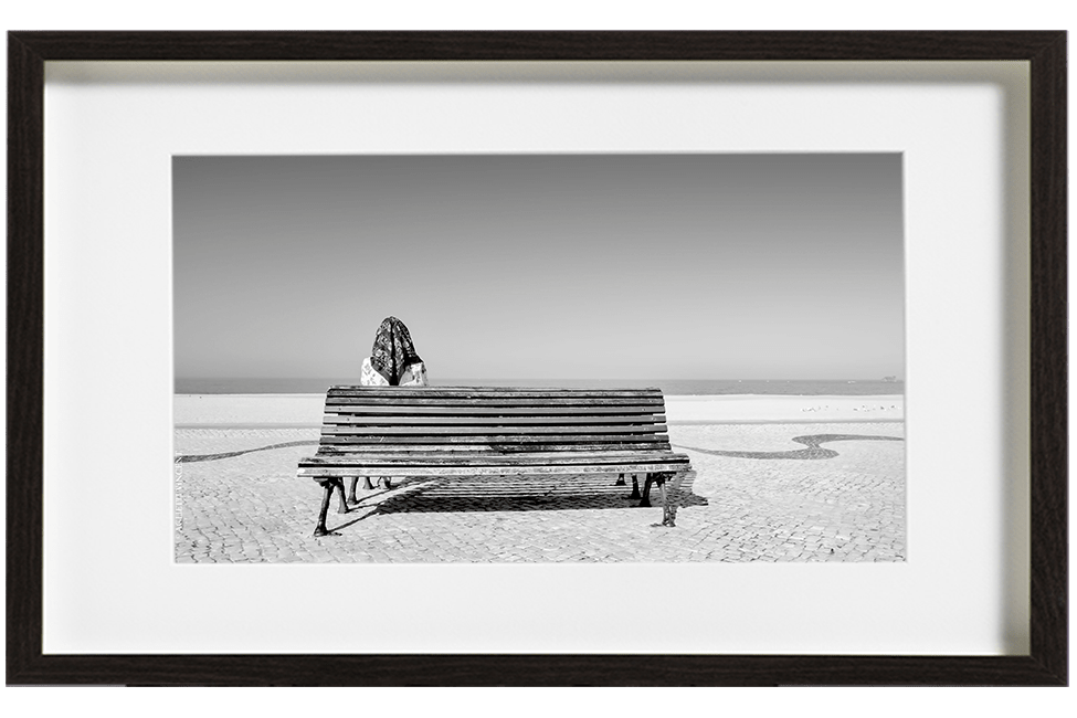 A Nazaré au Portugal, une femme assise sur un banc face à la mer, un foulard sur la tête. Au sol, une mosaïque en arabesque fuit devant elle.