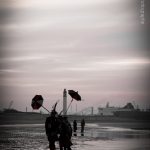 Une fin de bande, des carnavaleux déambulent sur la plage un berguenard sur l'épaule dans un contre jour. Le port de Dunkerque et ses cheminées en décor au fond de cette scène.