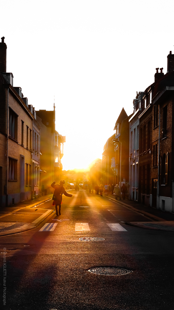 Fin de Carnaval. Un Carnavaleu dansant en traversant la rue. Le soleil.se couche sur Malo.