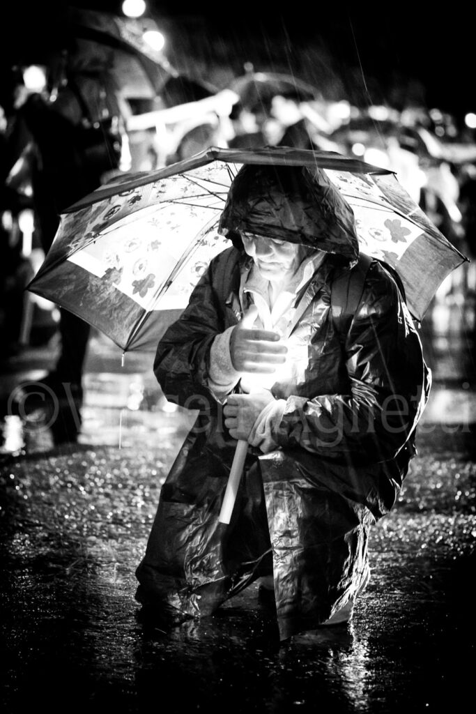 Pèlerin à genoux sous un parapluie écoutant les discours des évêques au sanctuaire de Fátima.