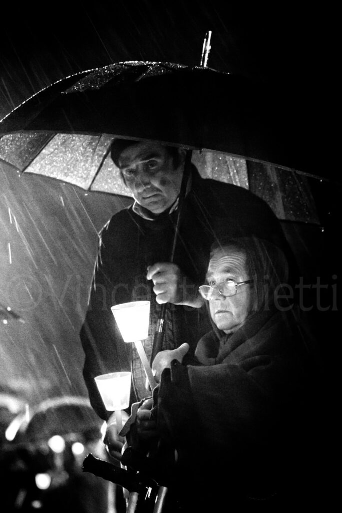 Couple de pèlerins assis sous un parapluie pendant la procession aux cierges sur l'esplanade du sanctuaire de Fátima.