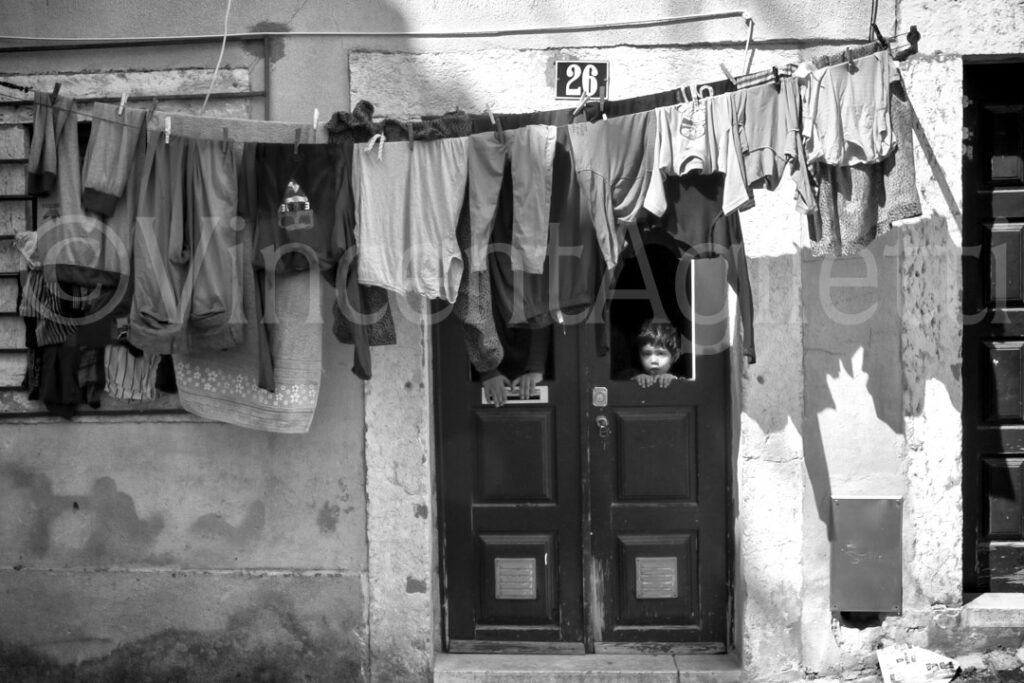 Deux enfants derrière une porte entourée de linge suspendu dans le quartier de la Mouraria à Lisbonne.