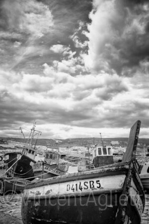 Bateaux de pêche à quai sur le port de Sesimbra à marée basse sous un ciel chargé.