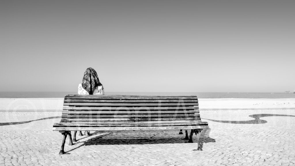 Une femme assise sur un banc face à l'océan à Nazaré au Portugal, photographie de la série Saudade.