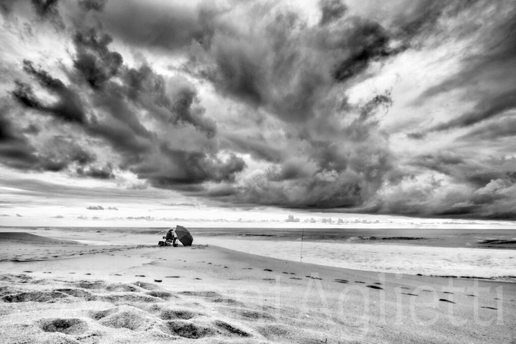 Pêcheur solitaire sur la plage de Melidés au Portugal sous un ciel menaçant, photographie en noir et blanc