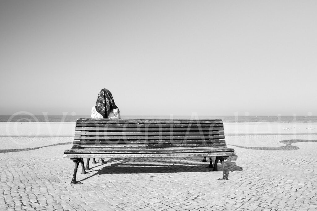 Une femme assise sur un banc face à l'océan à Nazaré, photographie de Street Photography au Portugal.