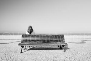 Une femme assise sur un banc face à l'océan à Nazaré, photographie de Street Photography au Portugal.