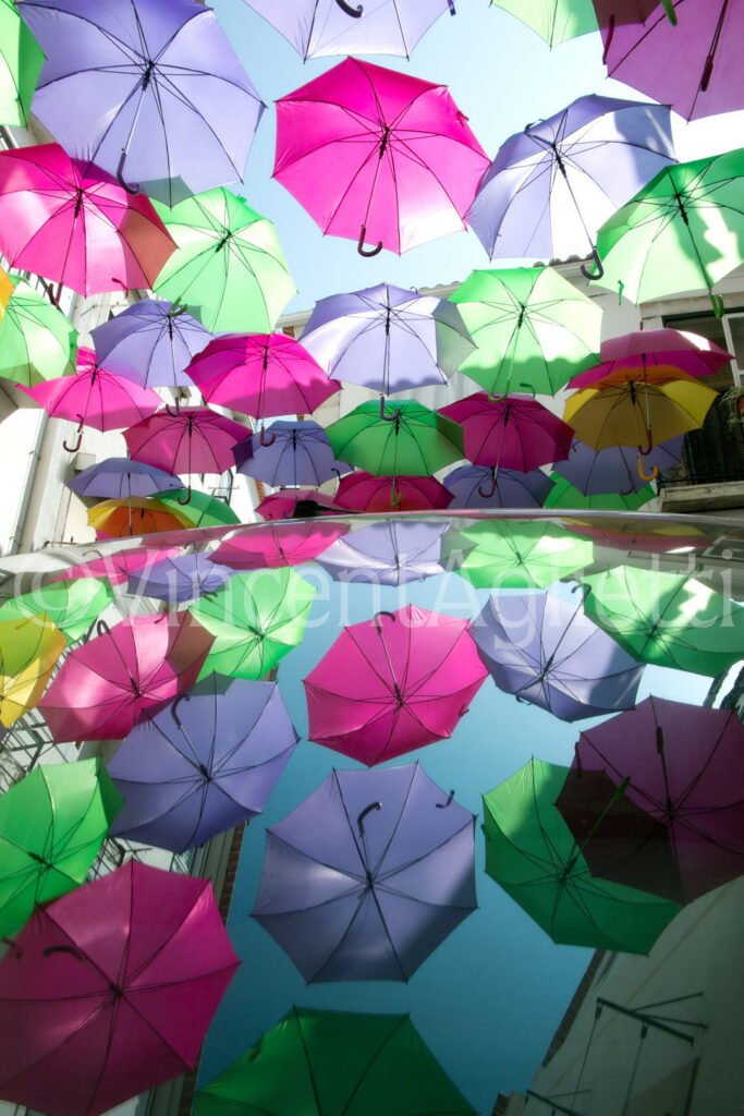 Parapluies colorés suspendus dans une rue d’Alfama et reflétés sur une carrosserie