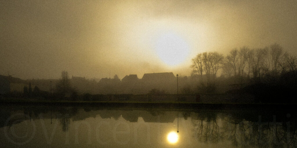 Canal traversant un village de Bourgogne sous la brume au lever du soleil